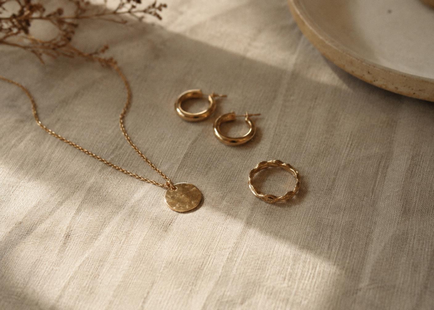 Gold necklace, hoops and a ring on warm linen